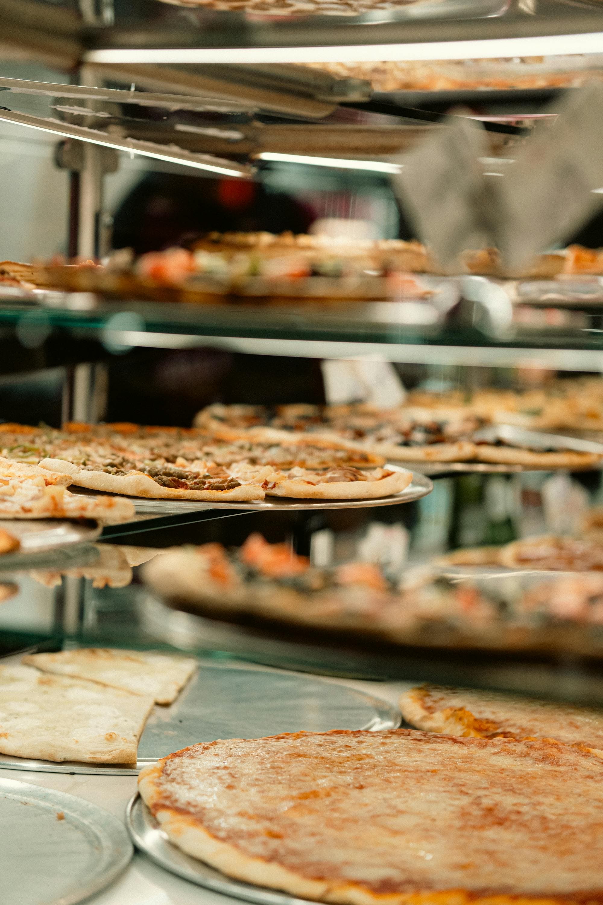 Whole pizzas stacked in a warm-lit counter display case