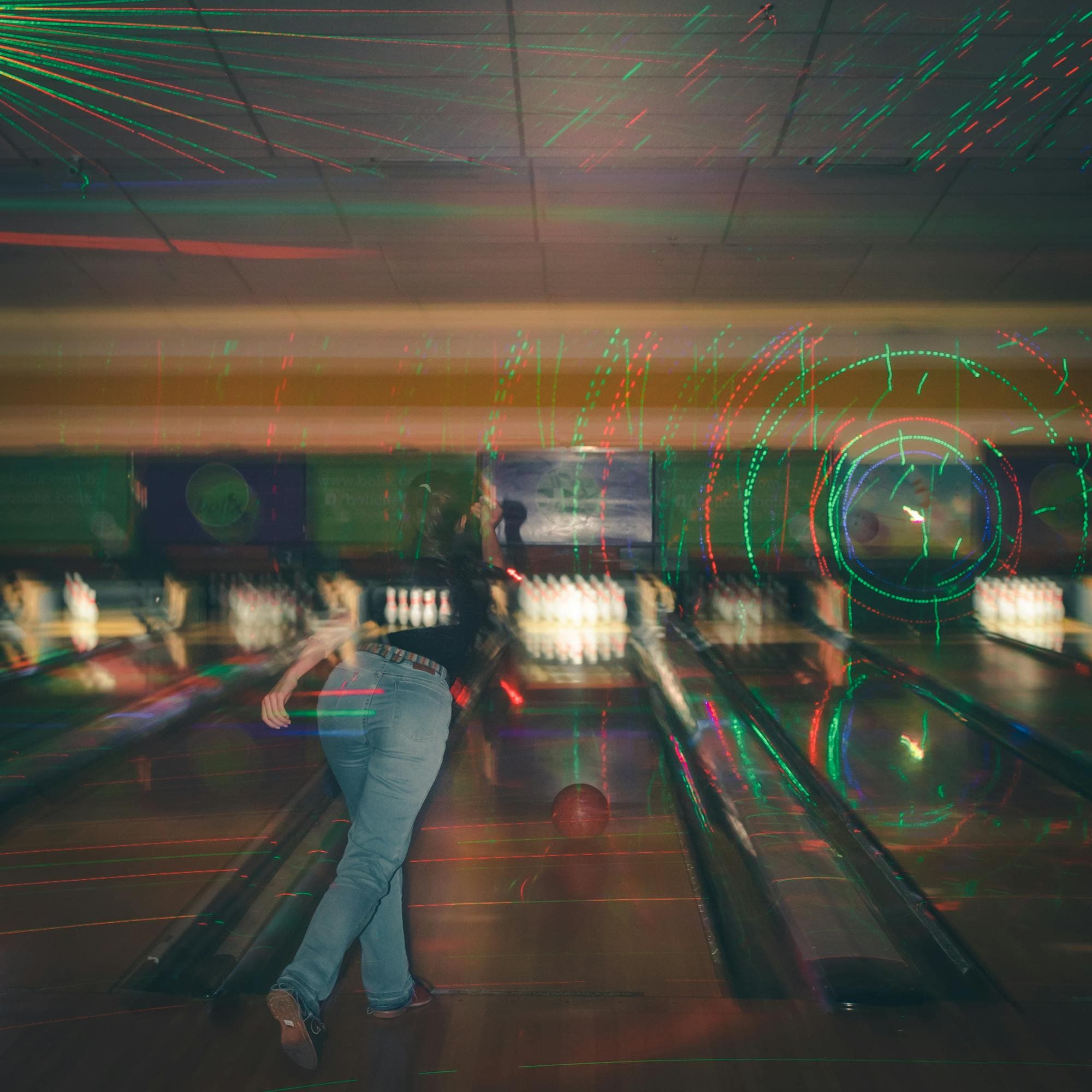 Bowler mid-throw under green and red glow-bowl lasers